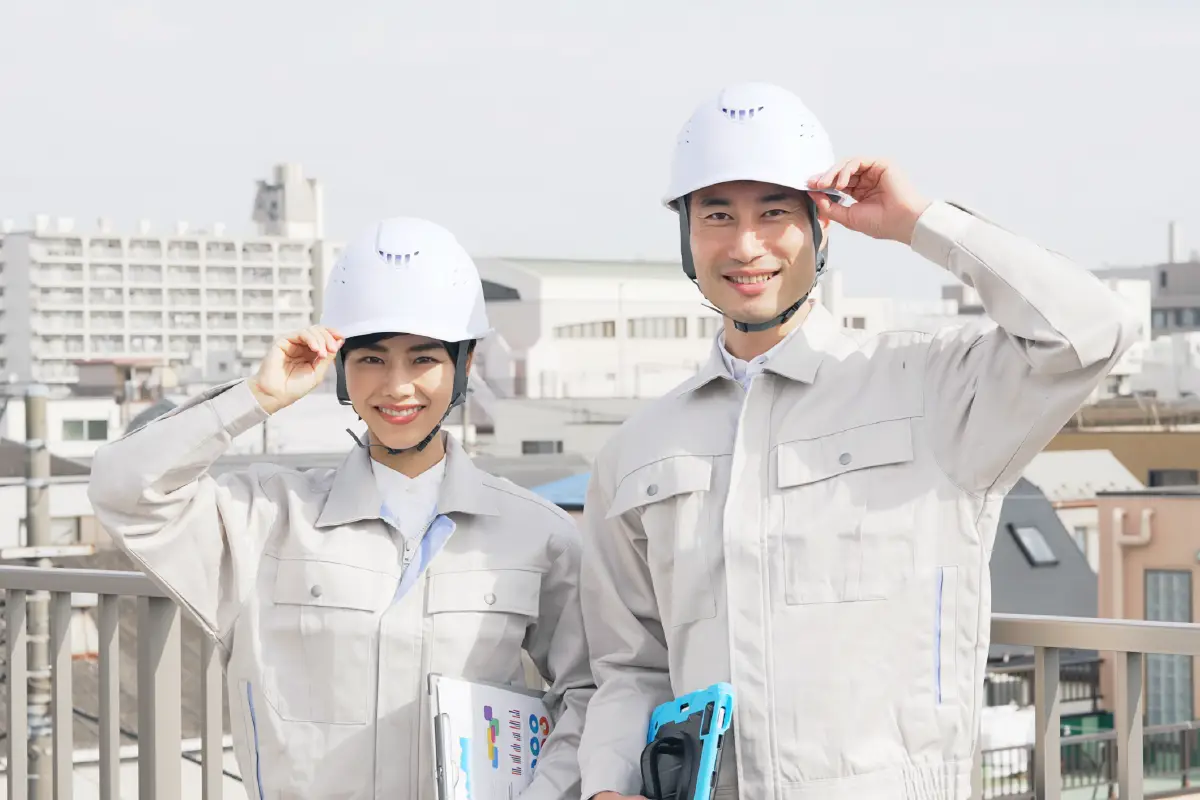 被っているヘルメットの縁をつまんでいる笑顔の男女の作業員